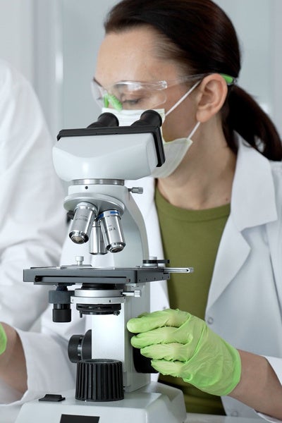Expert medical researcher examining samples with a scientific microscope, collaborating on pharmaceutical development and biological discovery in a modern laboratory setting