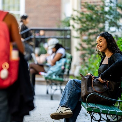 Manhattan University student smiling sitting on a bench talking to another student
