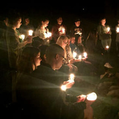 people seated in a circle at night, holding candles