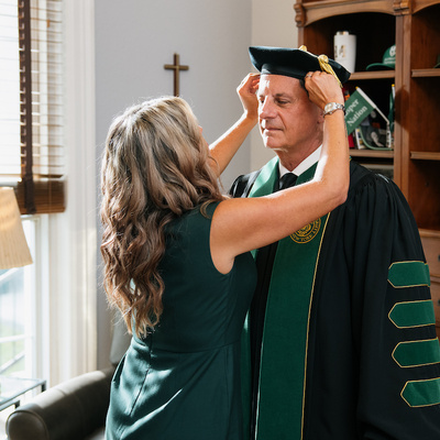 President Frederick Bonato prepares for inauguration with assistance adjusting academic cap.