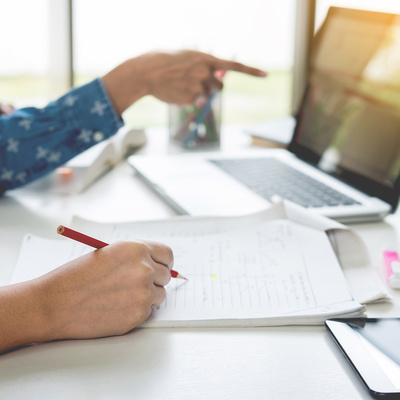 Student at table with laptop and person next to them with pencil and paper
