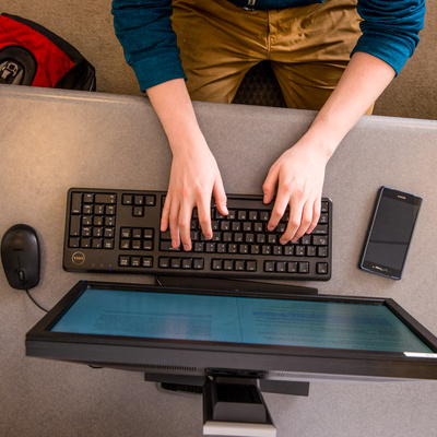 student's hands typing on computer keyboard from overhead view