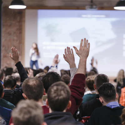 Adult students at large conference hall listen to a speaker.