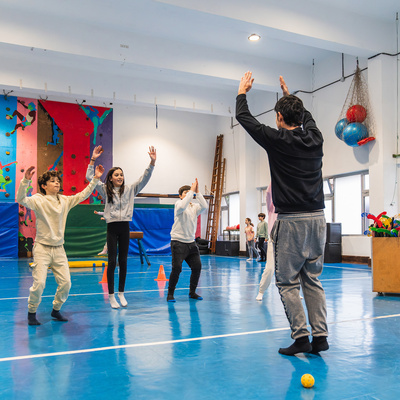 Students jumping and raising their arms, following their gym teacher's instructions during a physical education class