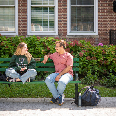 Manhattan University students sitting on a bench outside talking
